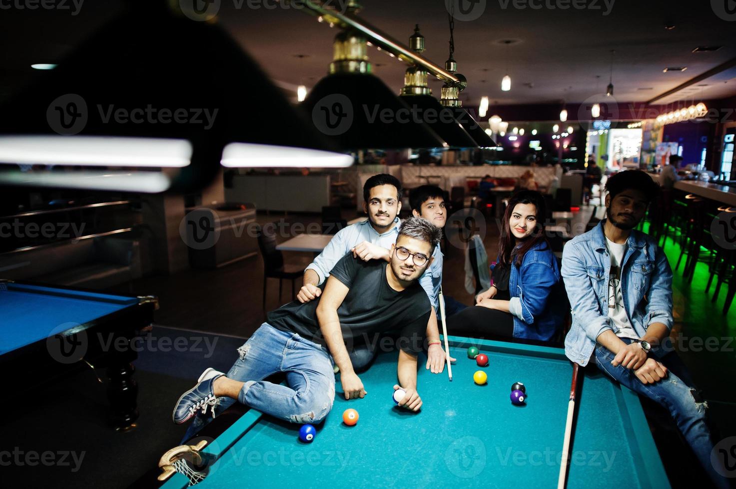 grupo de elegantes amigos asiáticos usan jeans jugando al billar en el bar. foto