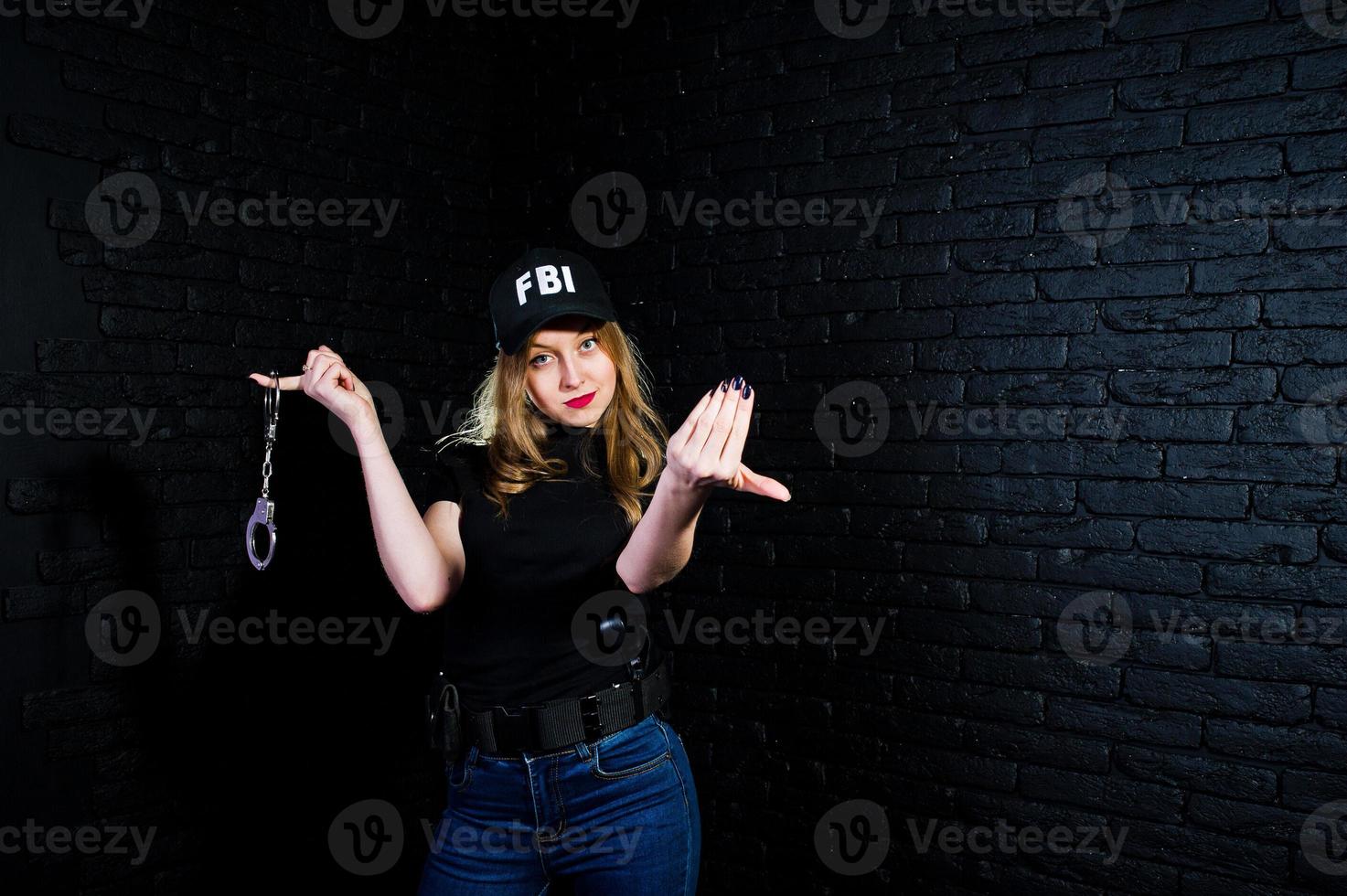 FBI female agent in cap and with gun at studio against dark brick wall. photo