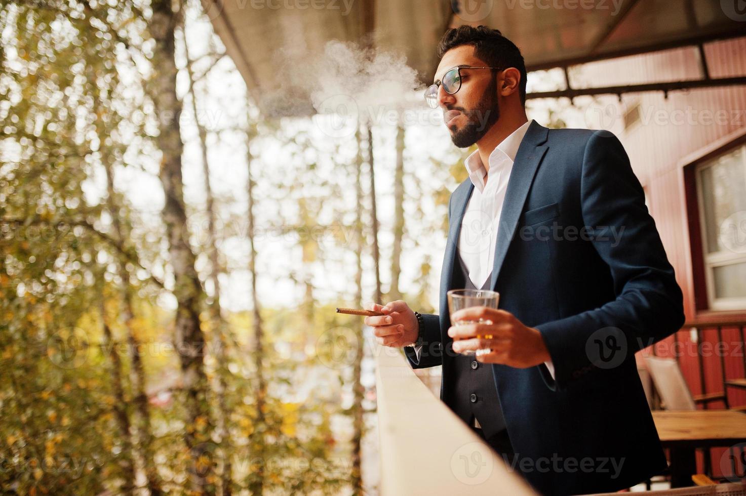 Handsome well-dressed arabian man smoke cigar at balcony of pub. photo