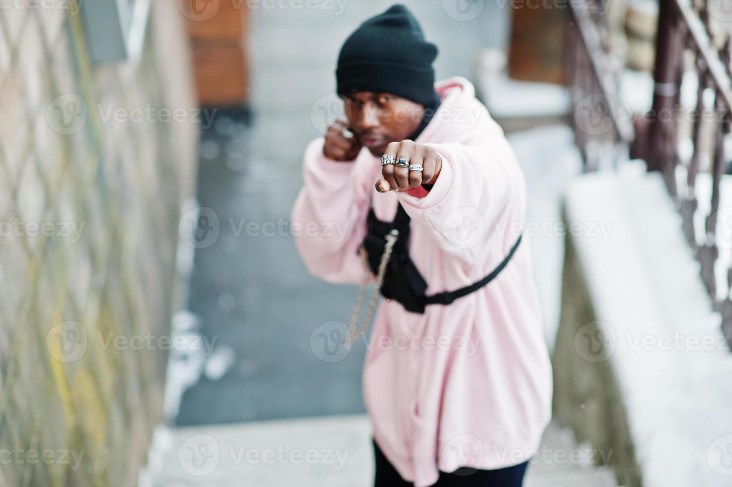 Elegante hombre afroamericano de estilo urbano con capucha rosa posado en el día de invierno y manos de boxeo. foto