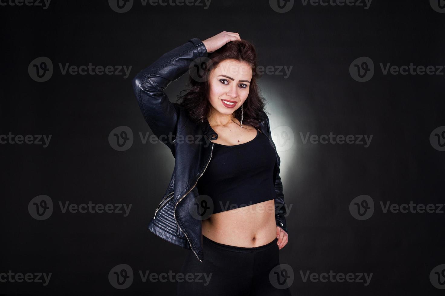 Studio portrait of sexy brunette girl in black leather jacket against black background. photo