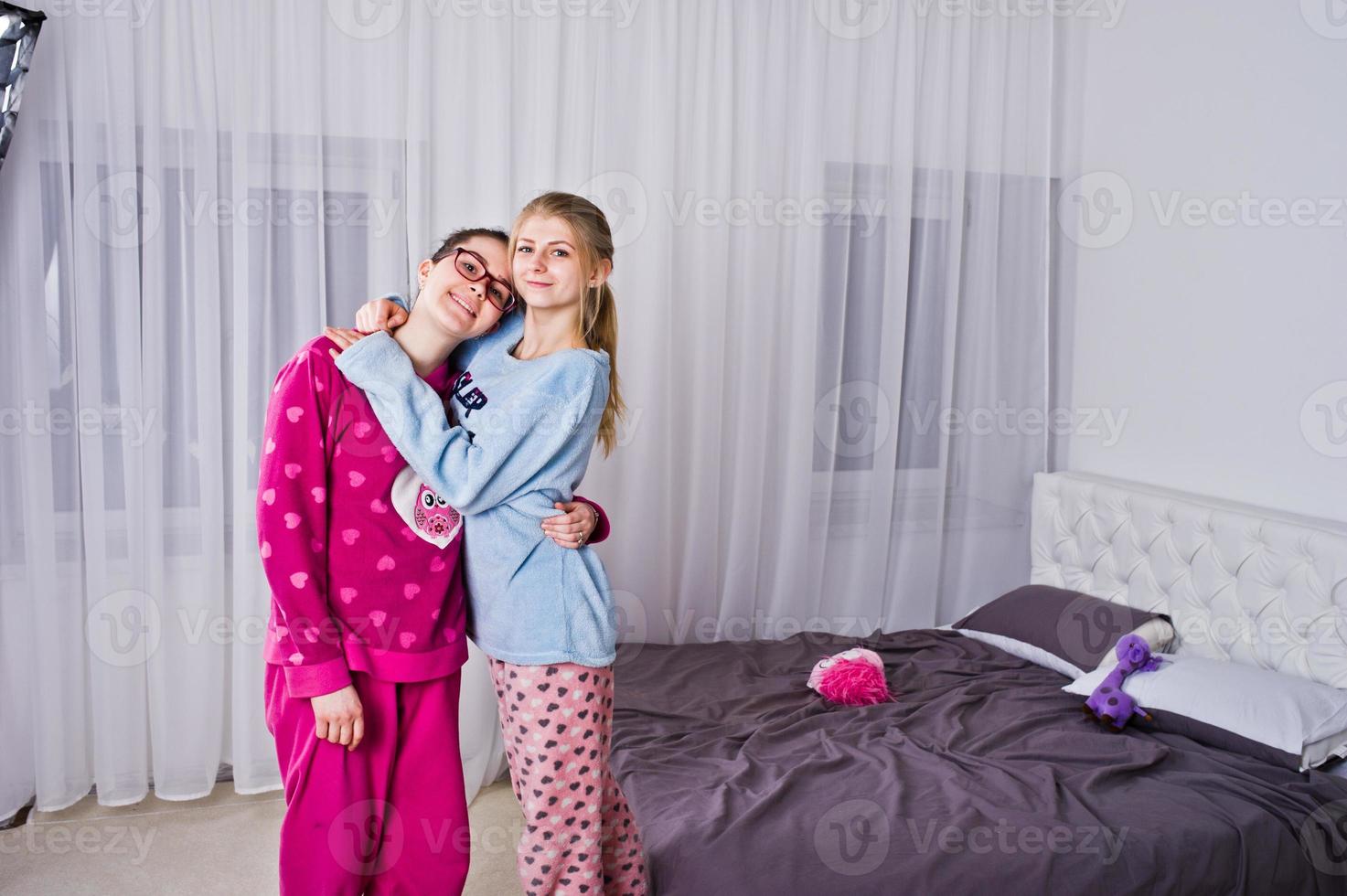 Two friends girls in pajamas having fun on bed at room. photo