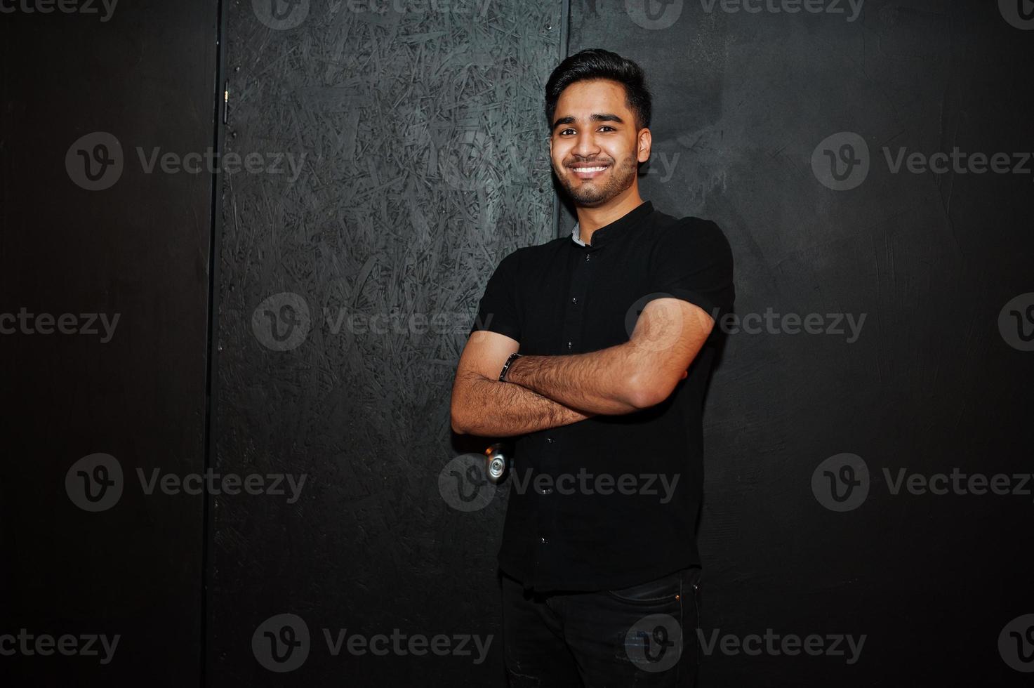 Asian man in black shirt on dark background posed with crossed arms. photo