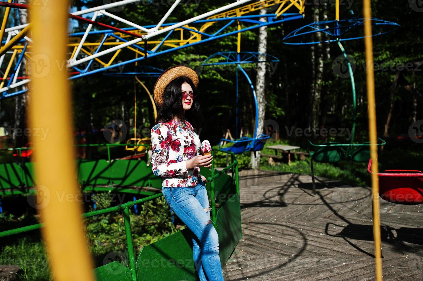 Portrait of brunette girl in pink glasses and hat with ice cream at amusement park. photo