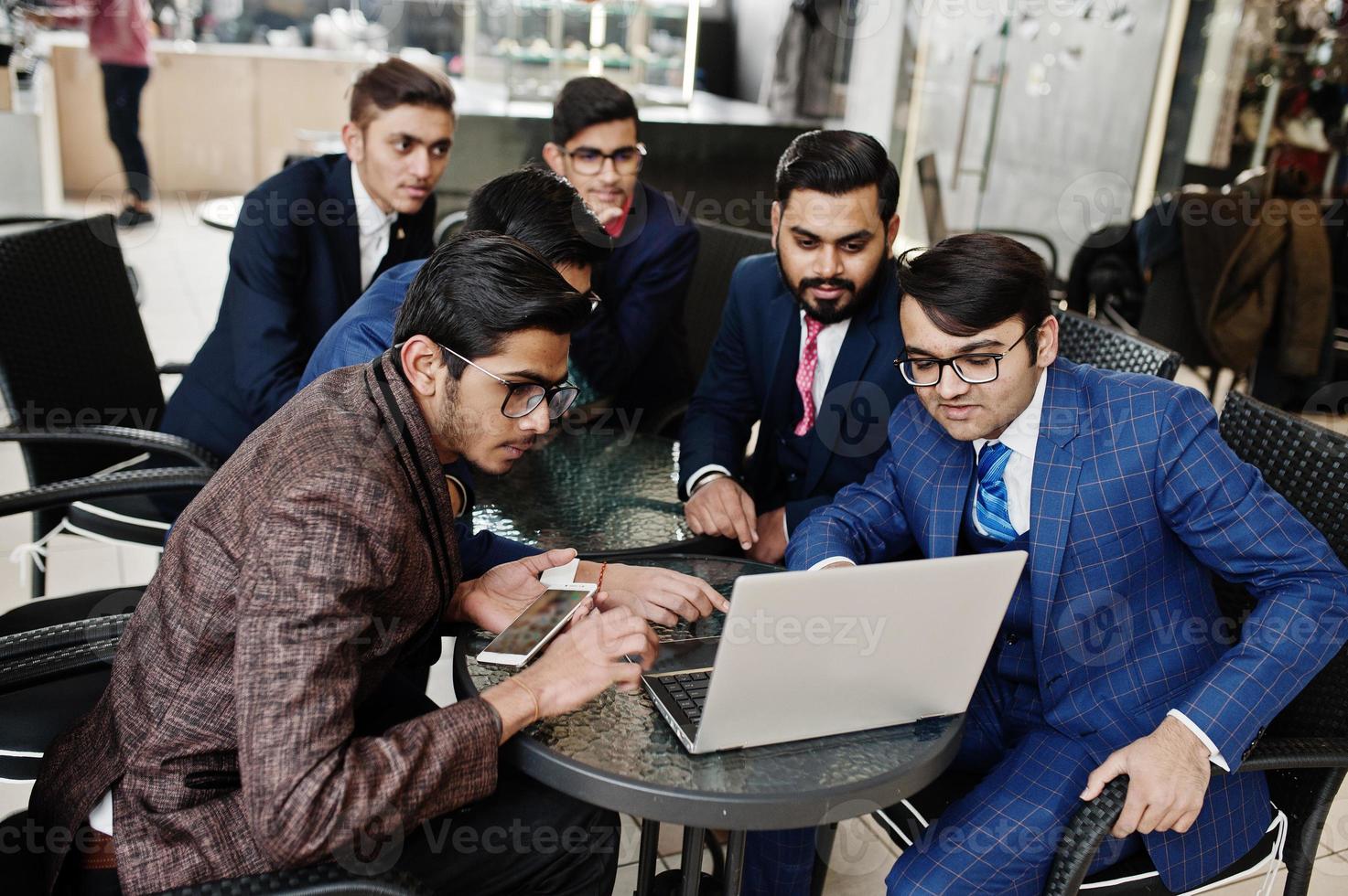 Group of six indian business man in suits sitting at office on cafe and looking at laptop. photo
