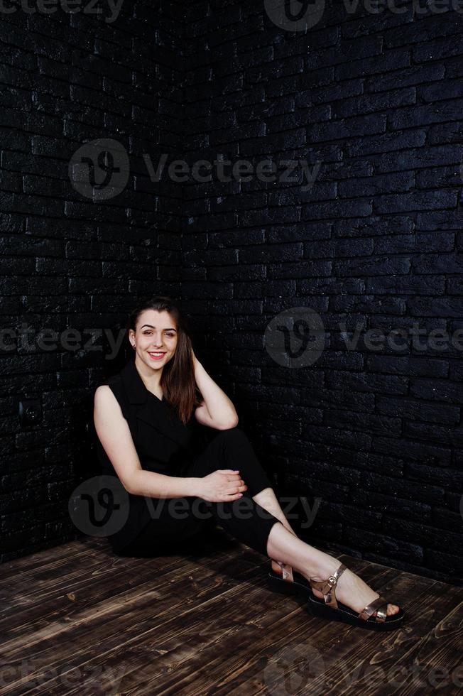 retrato de una hermosa morena con mono negro sentada y posando en el estudio. foto