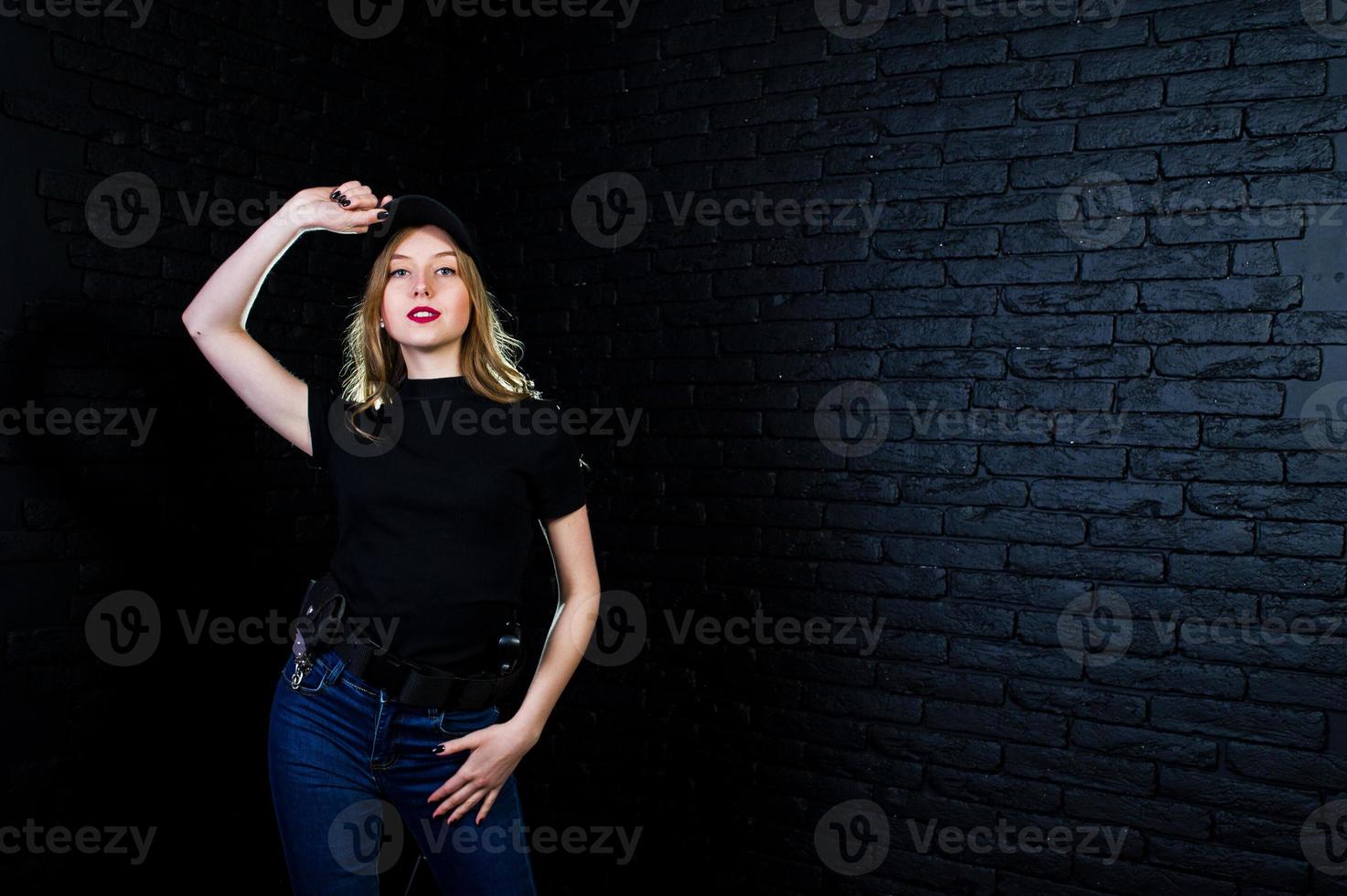 FBI female agent in cap and with gun at studio against dark brick wall. photo