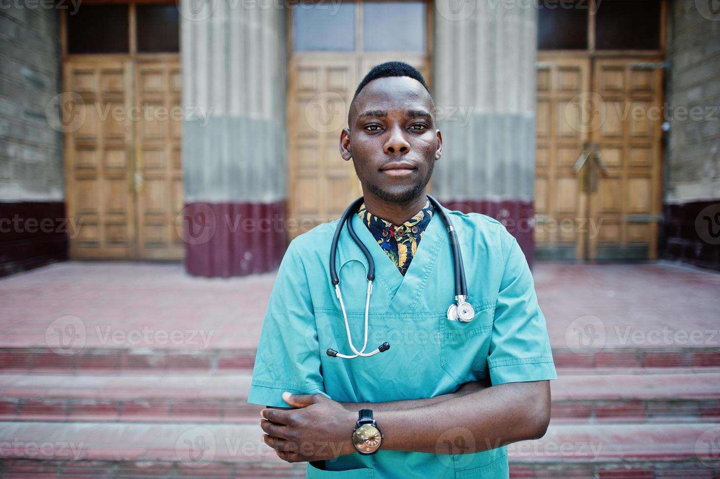 African american doctor male at lab coat with stethoscope outdoor against clinic door. photo