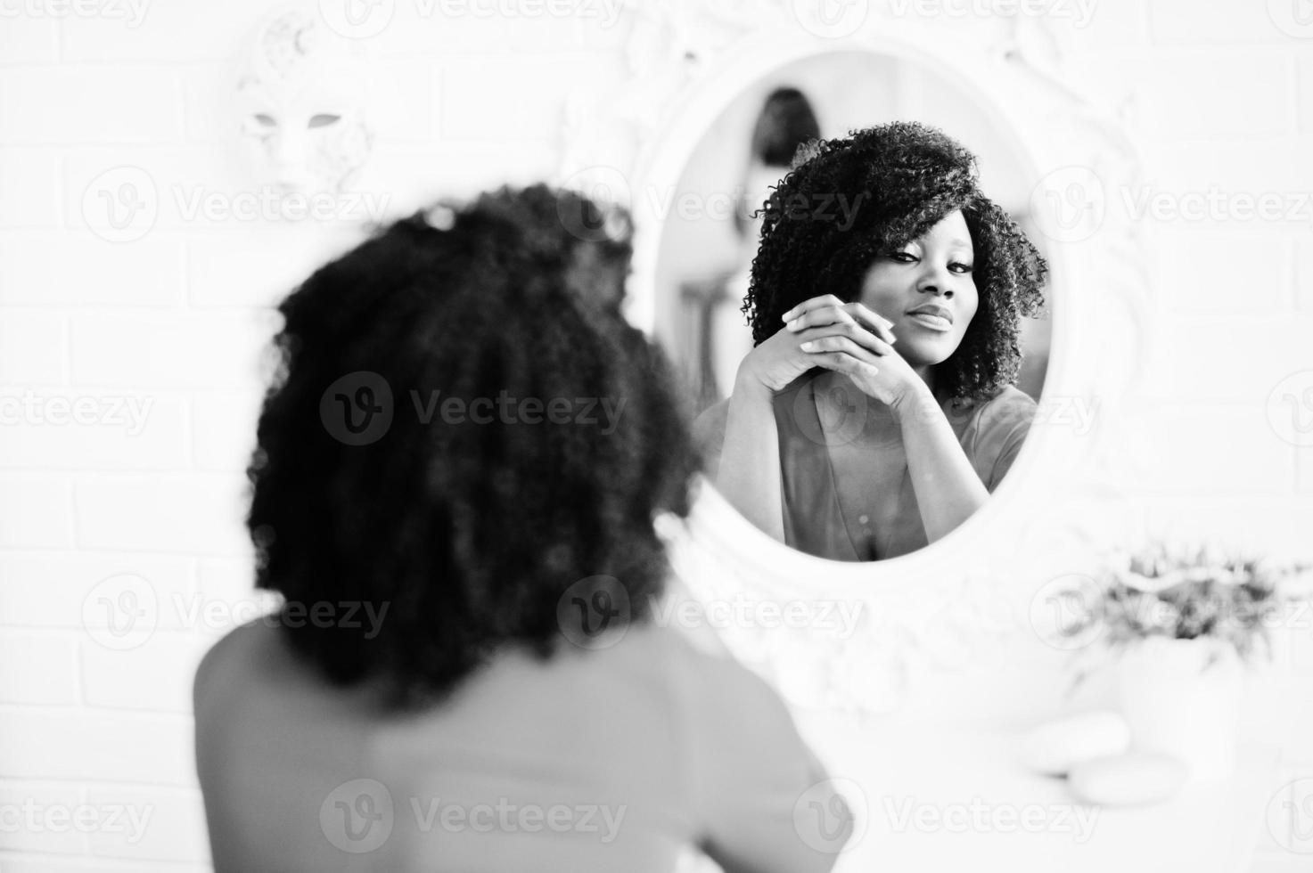 modelo afroamericano de moda en vestido de belleza rojo, mujer sexy posando vestido de noche y mirando al espejo. foto