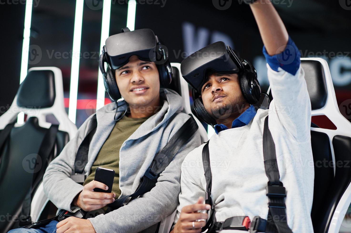 Two young indian people having fun with a new technology of a vr headset at virtual reality simulator and making selfie by mobile phone. photo