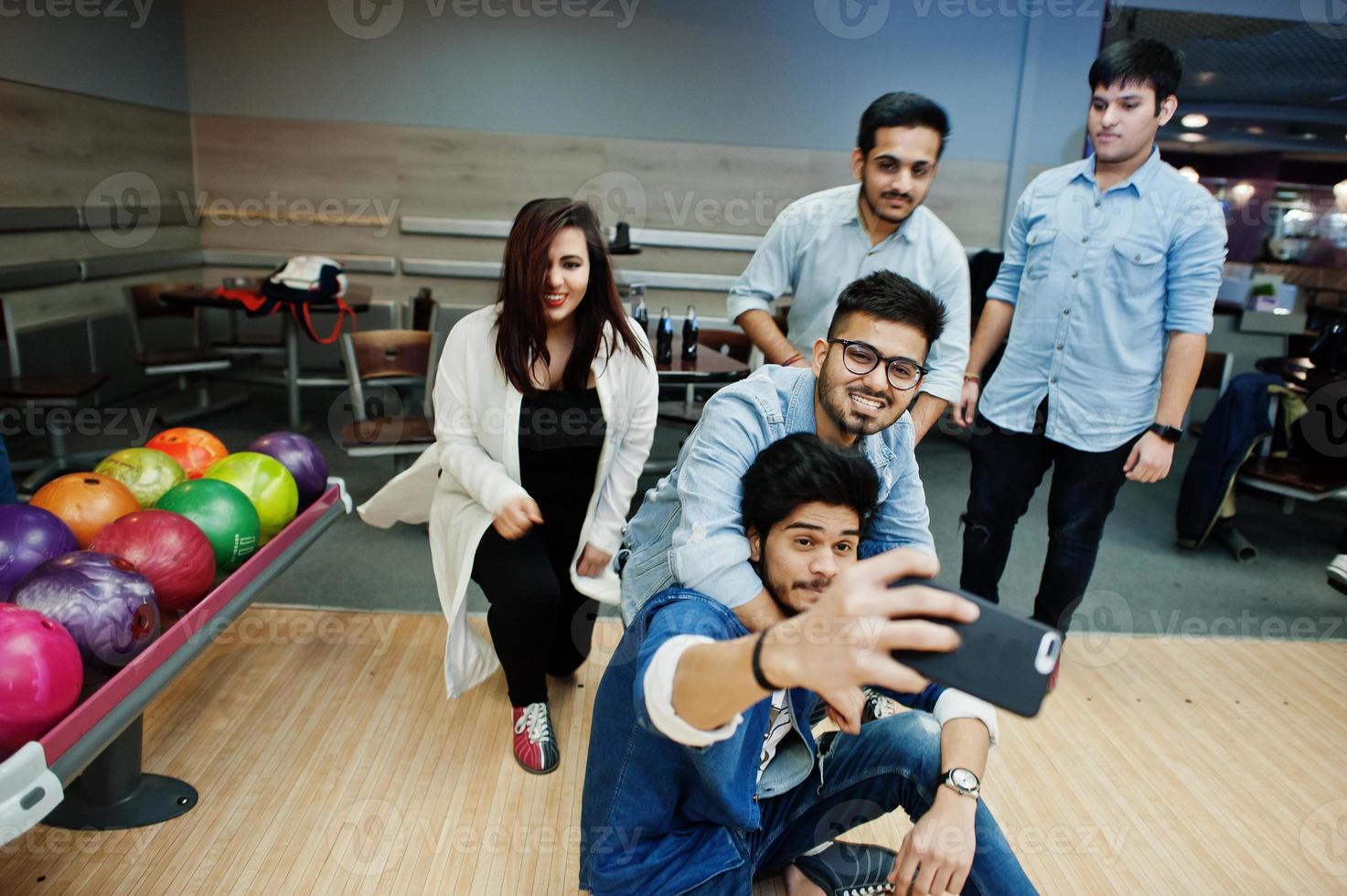 Group of five south asian peoples having rest and fun at bowling club. Making selfie by phone. photo