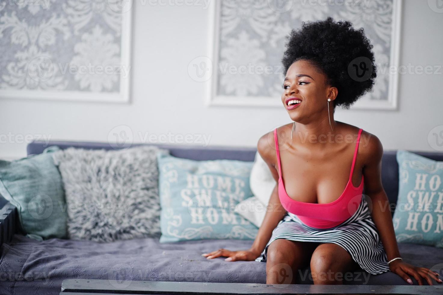 atractiva mujer afroamericana con cabello afro en la parte superior de la falda rosa, posada en la habitación blanca. modelo negro sexy de moda. foto