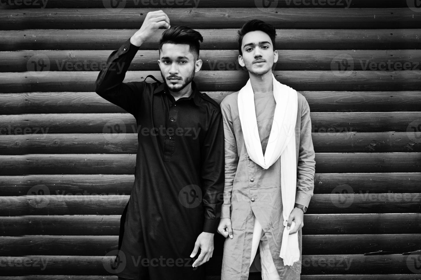 Two indian stylish mans friends in traditional clothes posed outdoor against wooden background. photo
