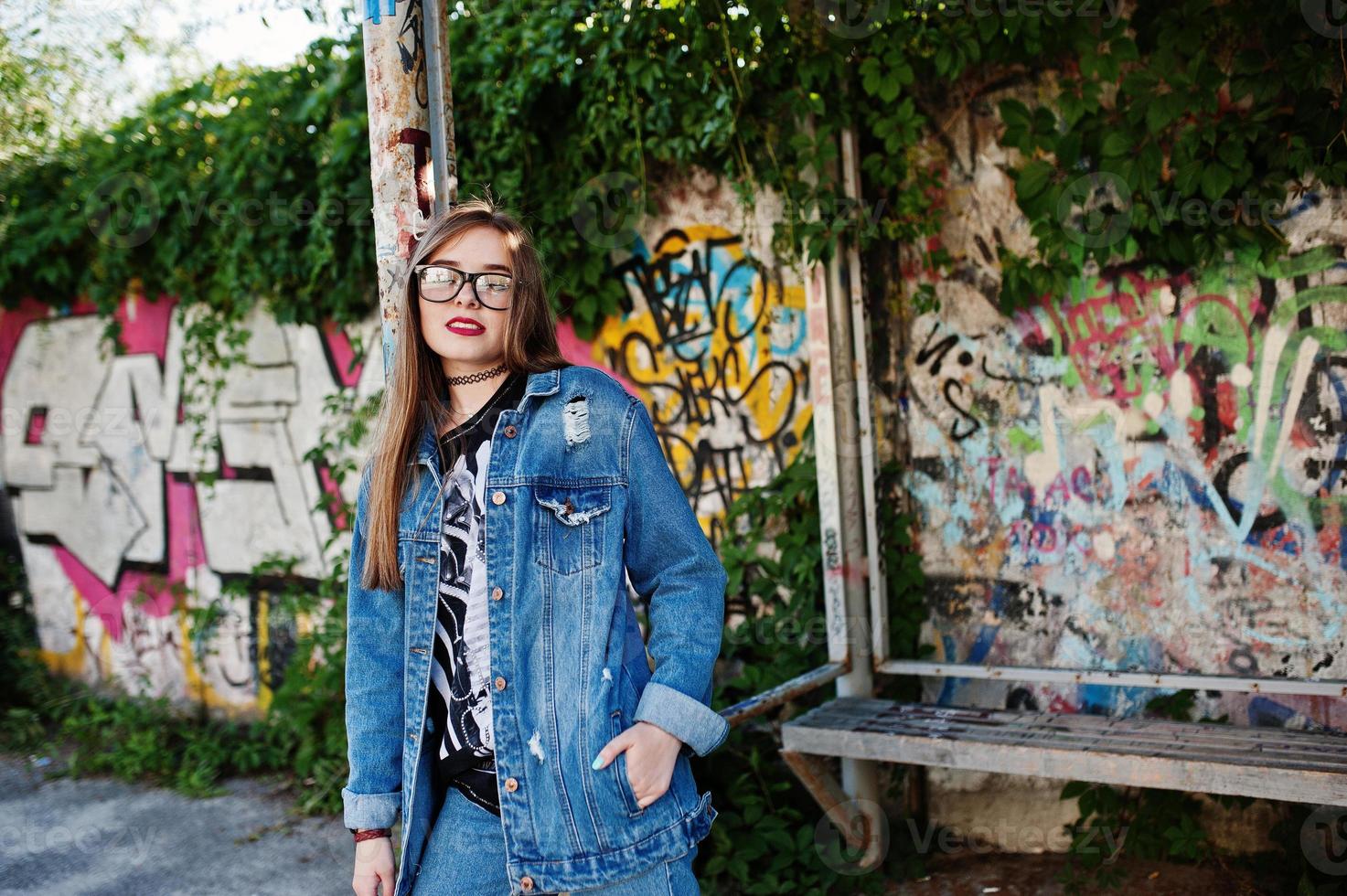 Stylish casual hipster girl in jeans wear and glasses against large graffiti wall. photo