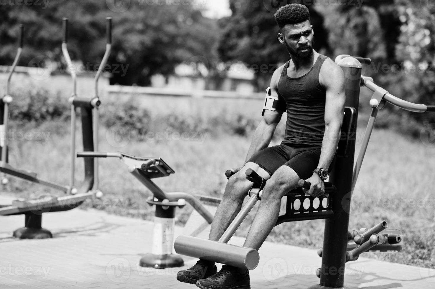 African american male athlete sport man with running sports arm case for mobile phone, doing exercises on the street workout simulators. photo