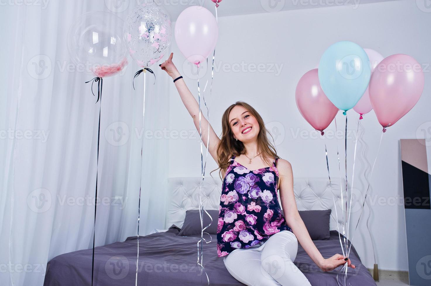 Happy girl with colored balloons on bed at room. Celebrating birthday theme. photo