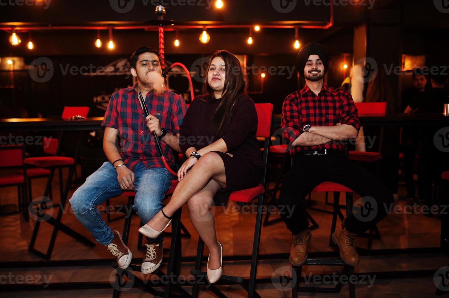 Group of indian friends sitting at lounge bar, smoke hookah and having rest. photo