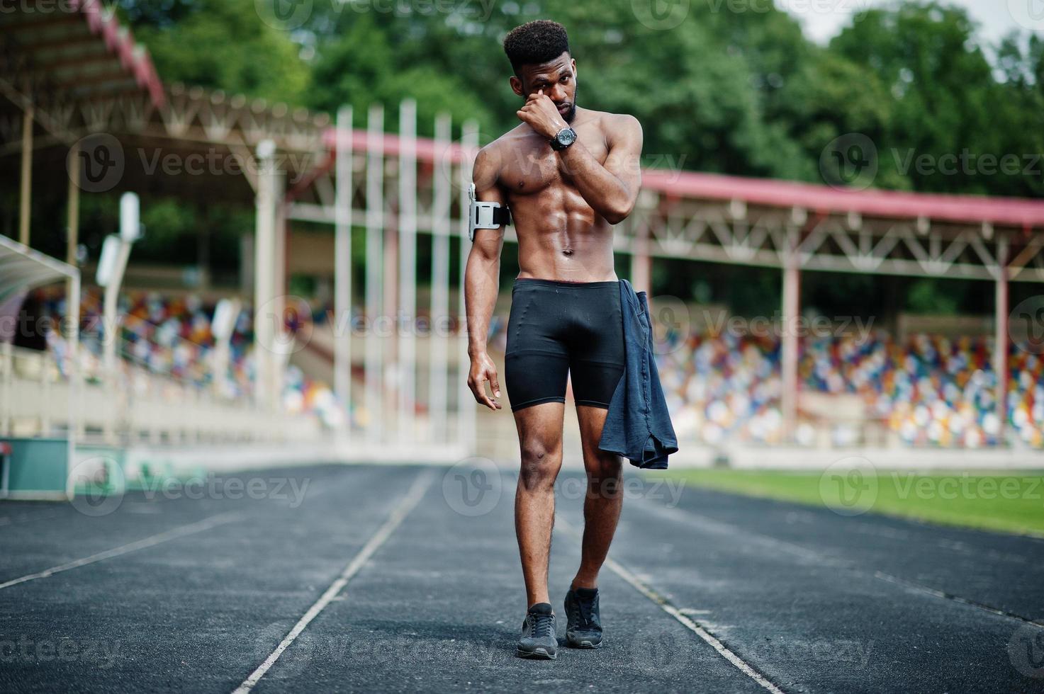 African american male athlete sexy sport bare torso man with running sports arm case for mobile phone, posed at stadium. photo