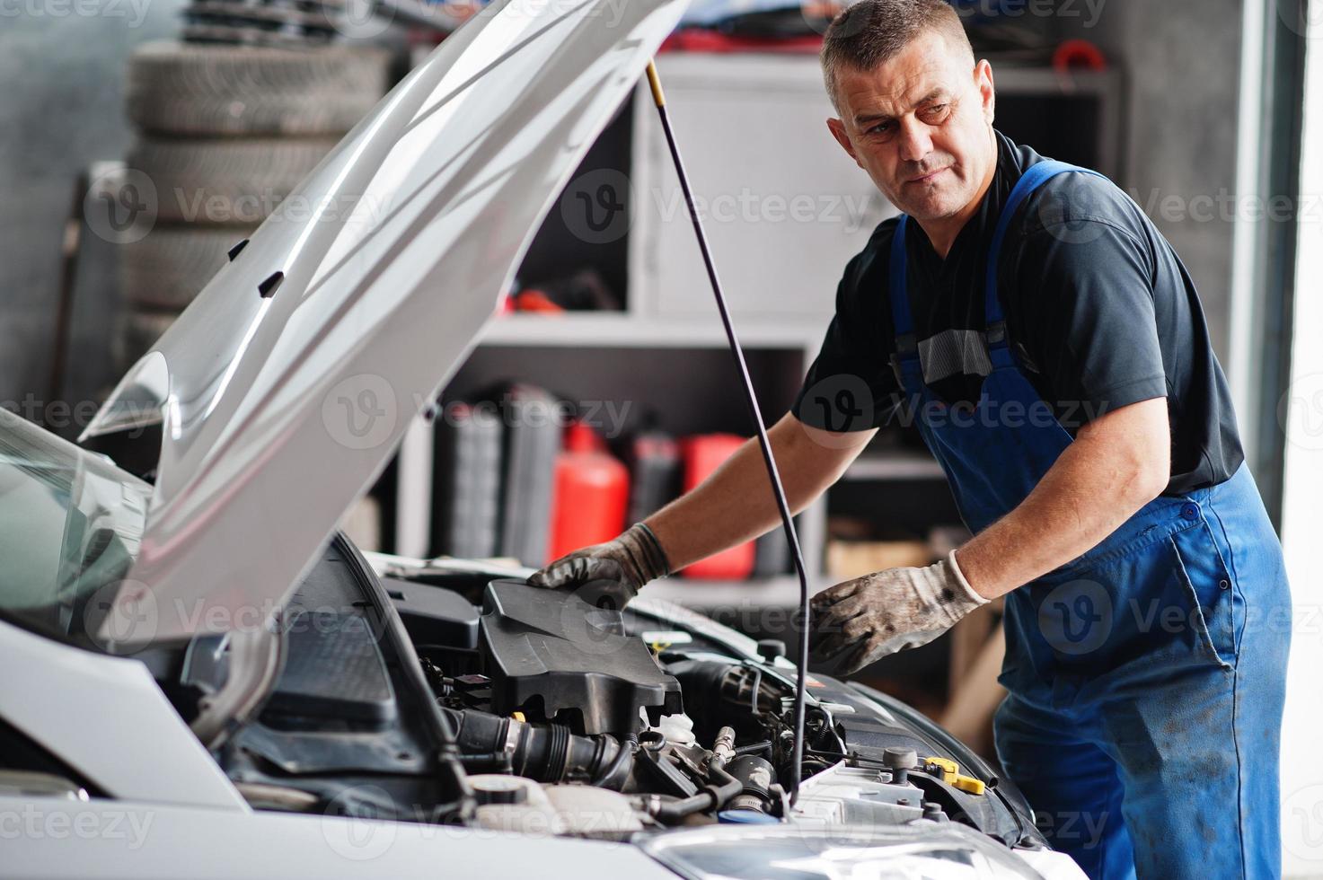 Car repair and maintenance theme. Mechanic in uniform working in auto service, checking engine. photo