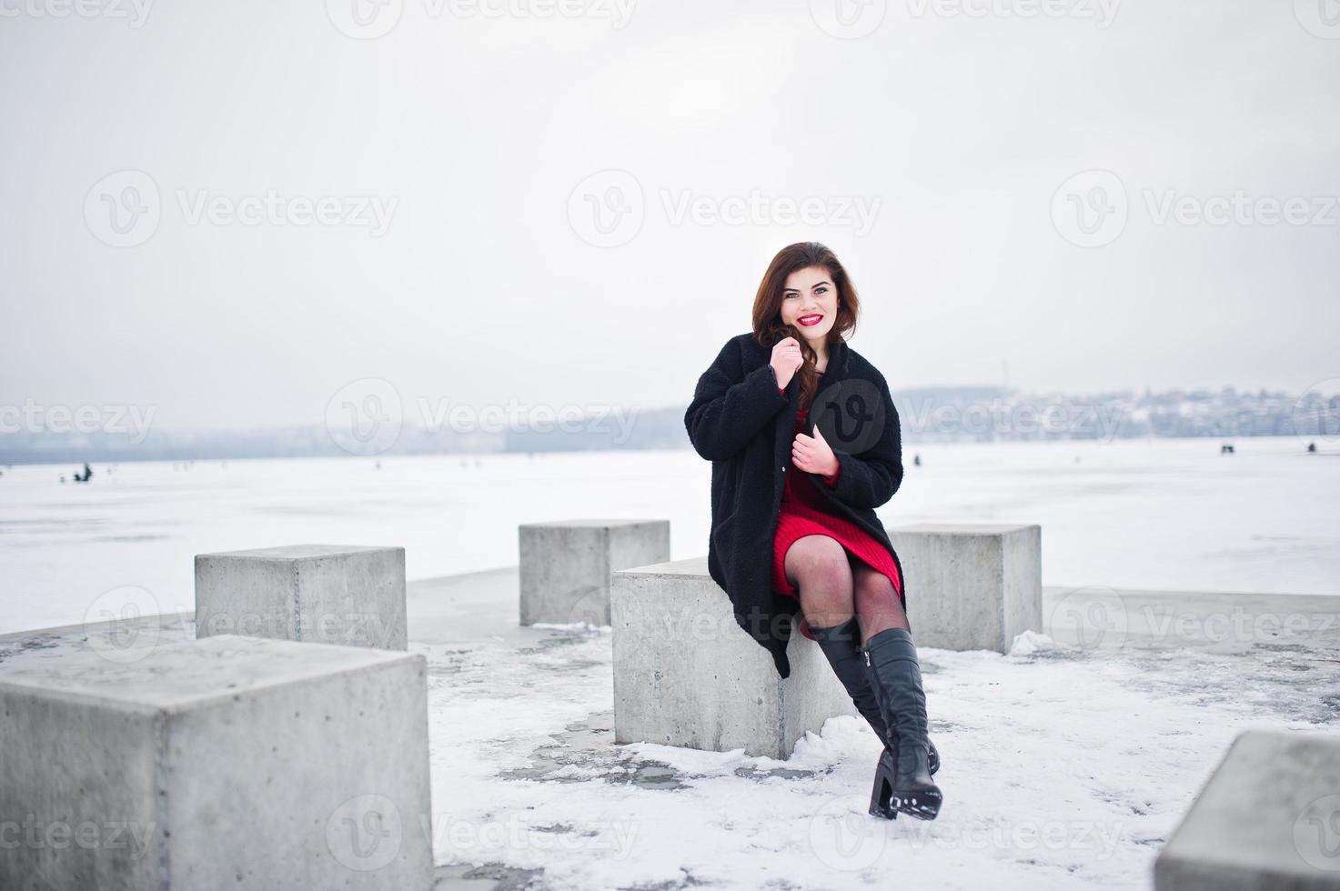 Brunette plus size model at red against frozen lake on winter day. photo