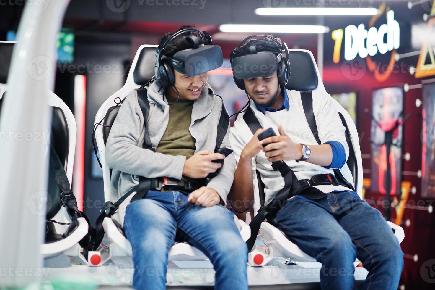 Two young indian people having fun with a new technology of a vr headset at virtual reality simulator with mobile phone at hands. photo