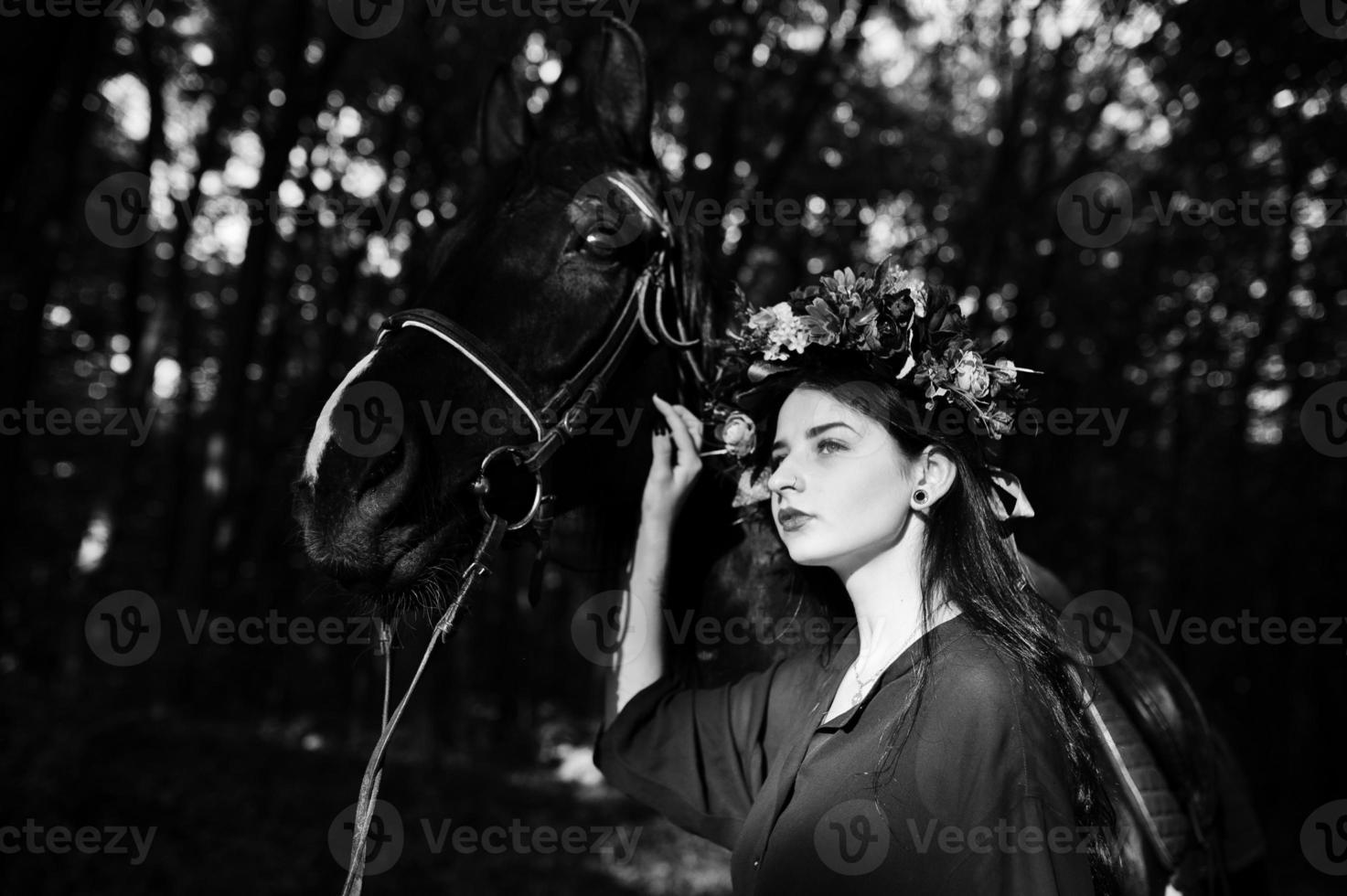 Mystical girl in wreath wear in black with horse in wood. photo