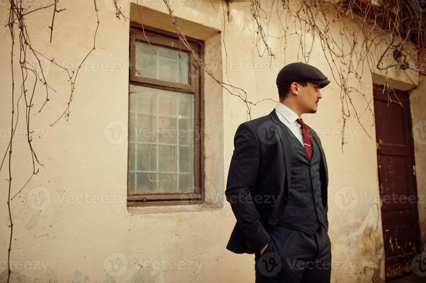Portrait of retro 1920s english arabian business man wearing dark suit, tie and flat cap. photo