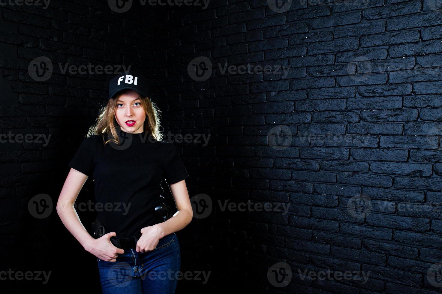 FBI female agent in cap and with gun at studio against dark brick wall. photo