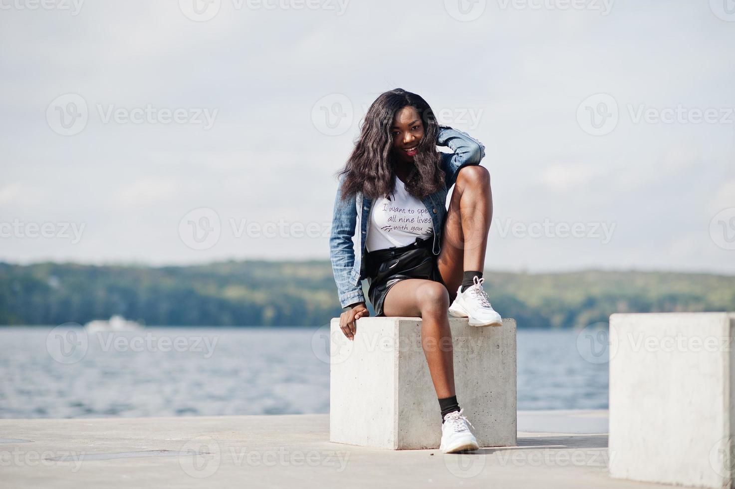 African american dark skinned slim model posed in a black shorts and jeans jacket against sea side. photo