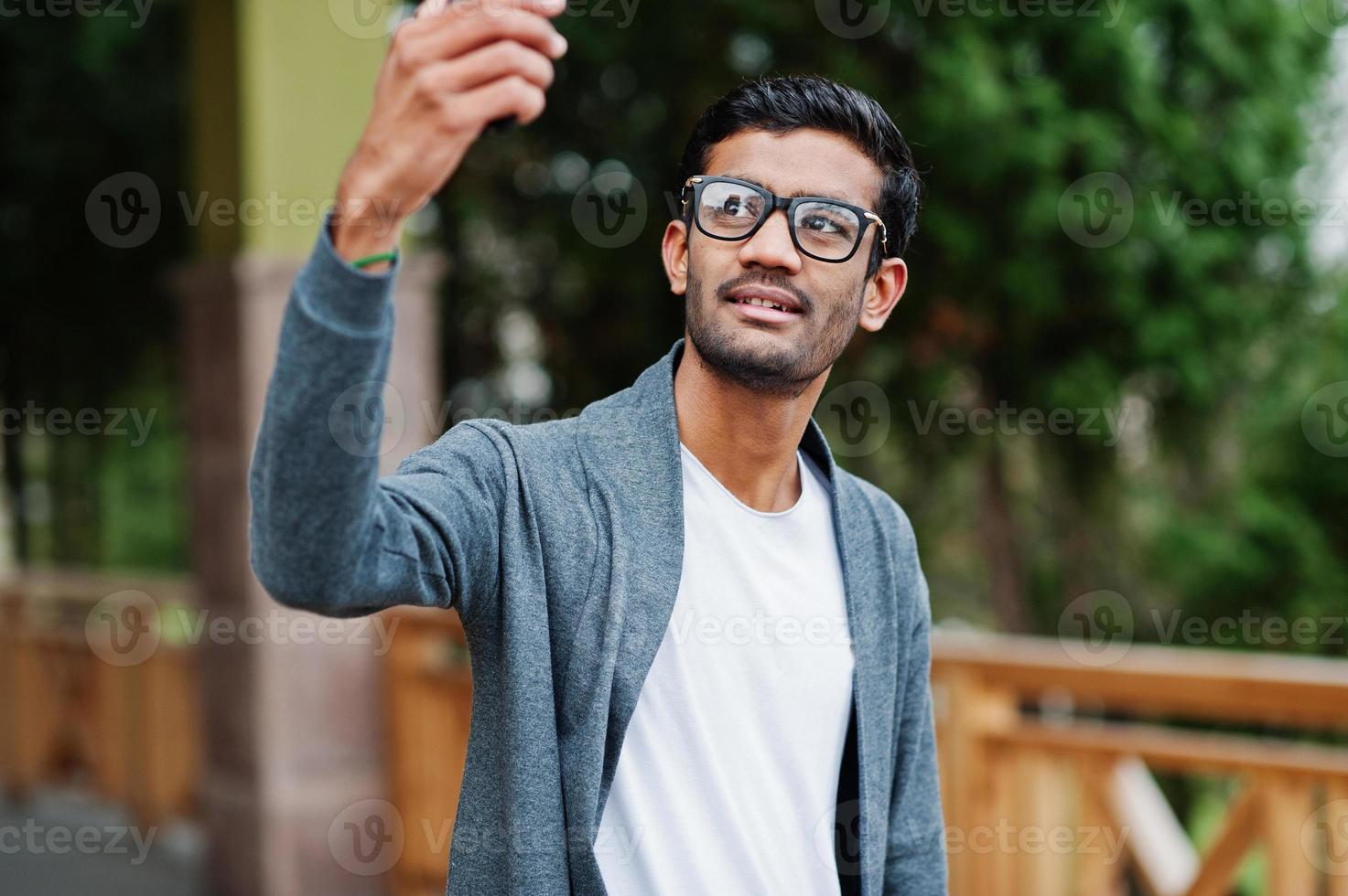 Stylish indian man at glasses wear casual posed outdoor and making selfie on phone. photo