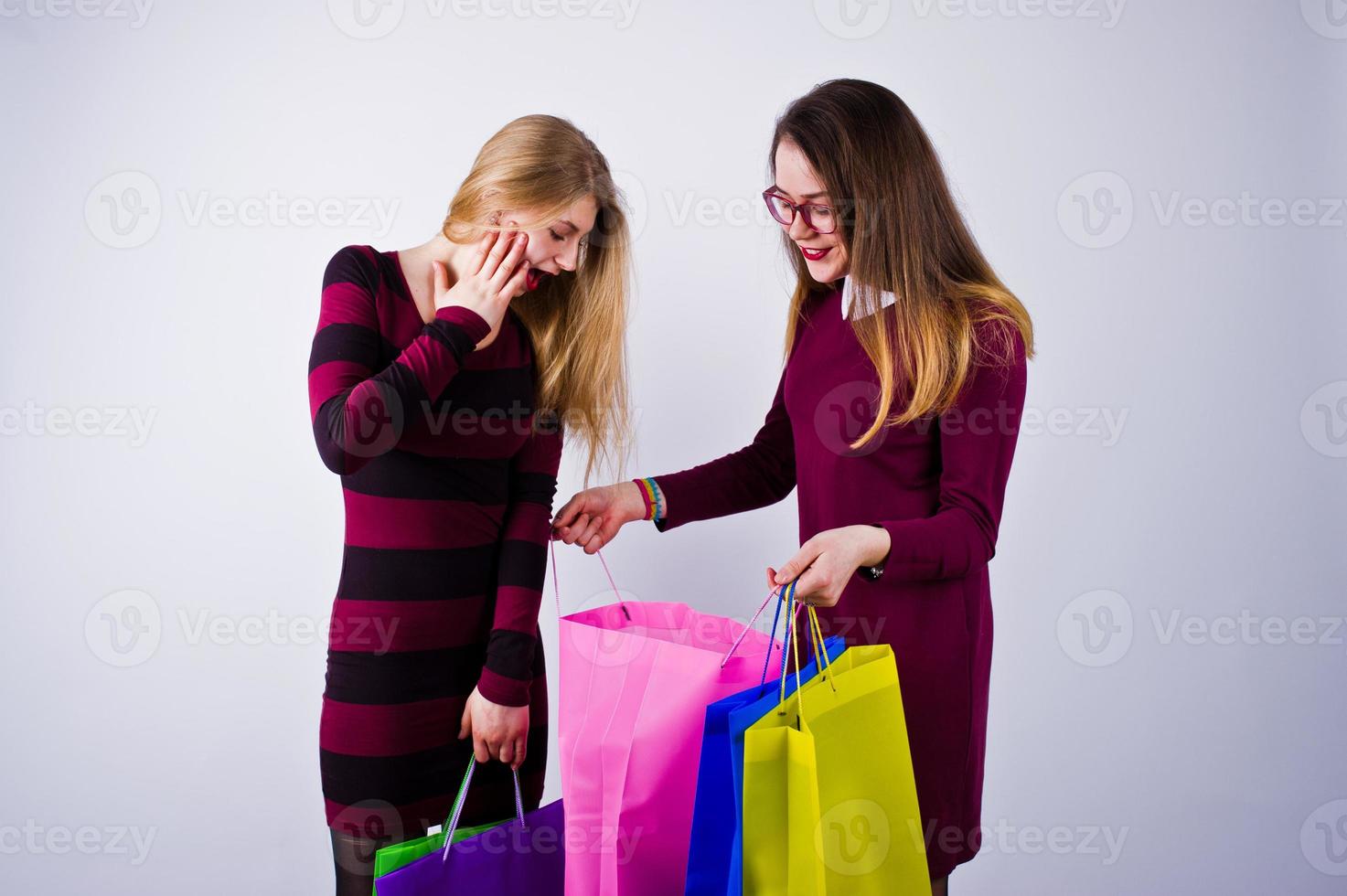 Two beautiful friends in cherry dresses posing with multicolored shopping bags in the studio. photo