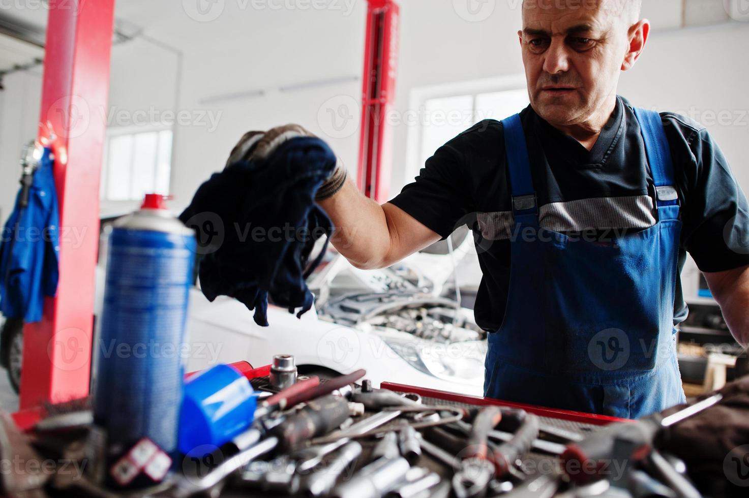 Car repair and maintenance theme. Mechanic in uniform working in auto service. photo