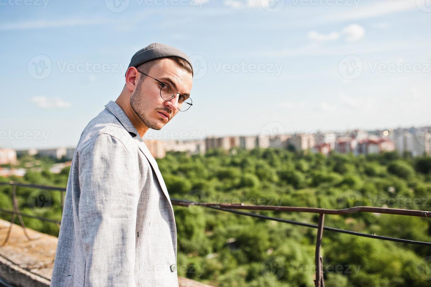 Dreamer stylish macho man in gray suit, hat and glasses posed on the roof. photo