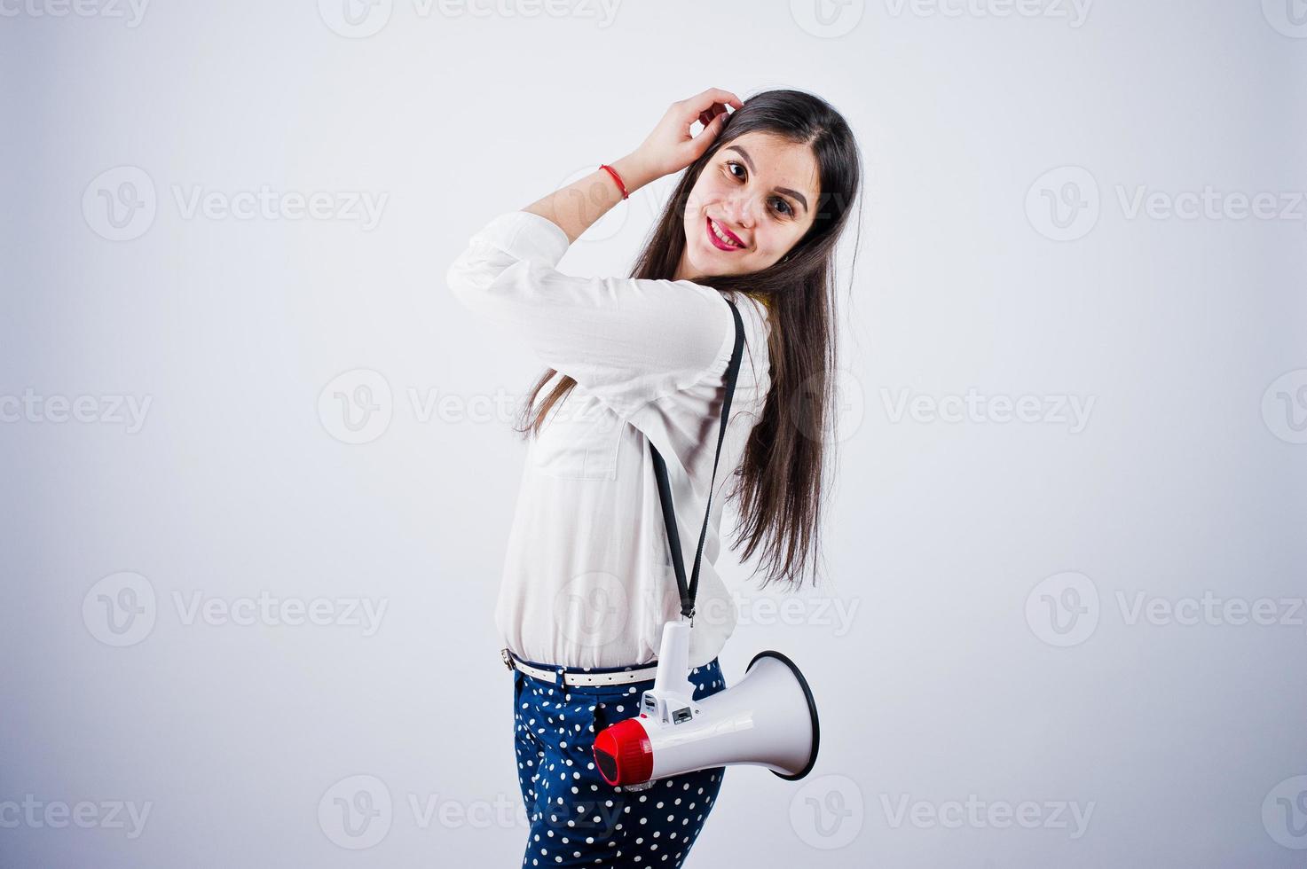 Portrait of a young woman in blue trousers and white blouse posing with megaphone in the studio. photo