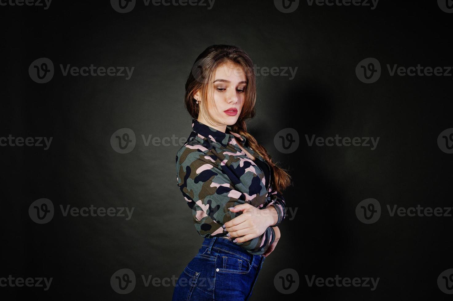 una guapa morena usa camisa militar y jeans, posando en el estudio con fondo gris. retrato de modelo de estudio. foto