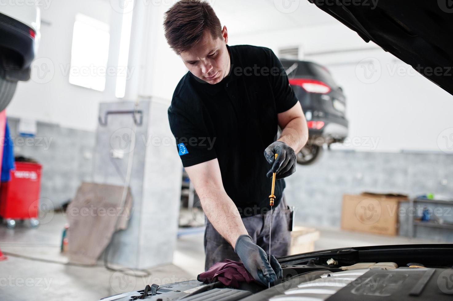 Car repair and maintenance theme. Mechanic in uniform working in auto service, checking engine. photo