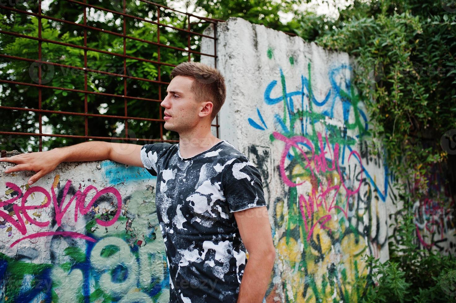 Lifestyle portrait of handsome man posing on the street of city with graffiti wall. photo