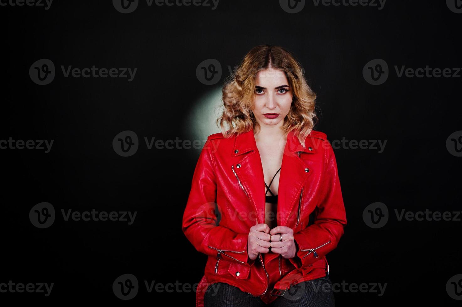 Studio portrait of blonde girl in red leather jacket against black background. photo