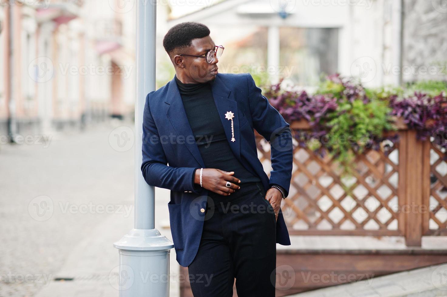 un hombre afroamericano de aspecto asombroso usa un blazer azul con broche,  cuello alto negro y anteojos posados en la calle. chico negro de moda.  10497584 Foto de stock en Vecteezy