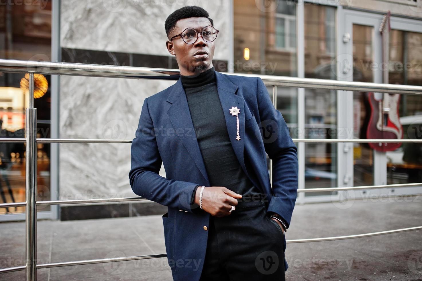 un hombre afroamericano de aspecto asombroso usa un blazer azul con broche,  cuello alto negro y anteojos posados en la calle. chico negro de moda.  10497590 Foto de stock en Vecteezy