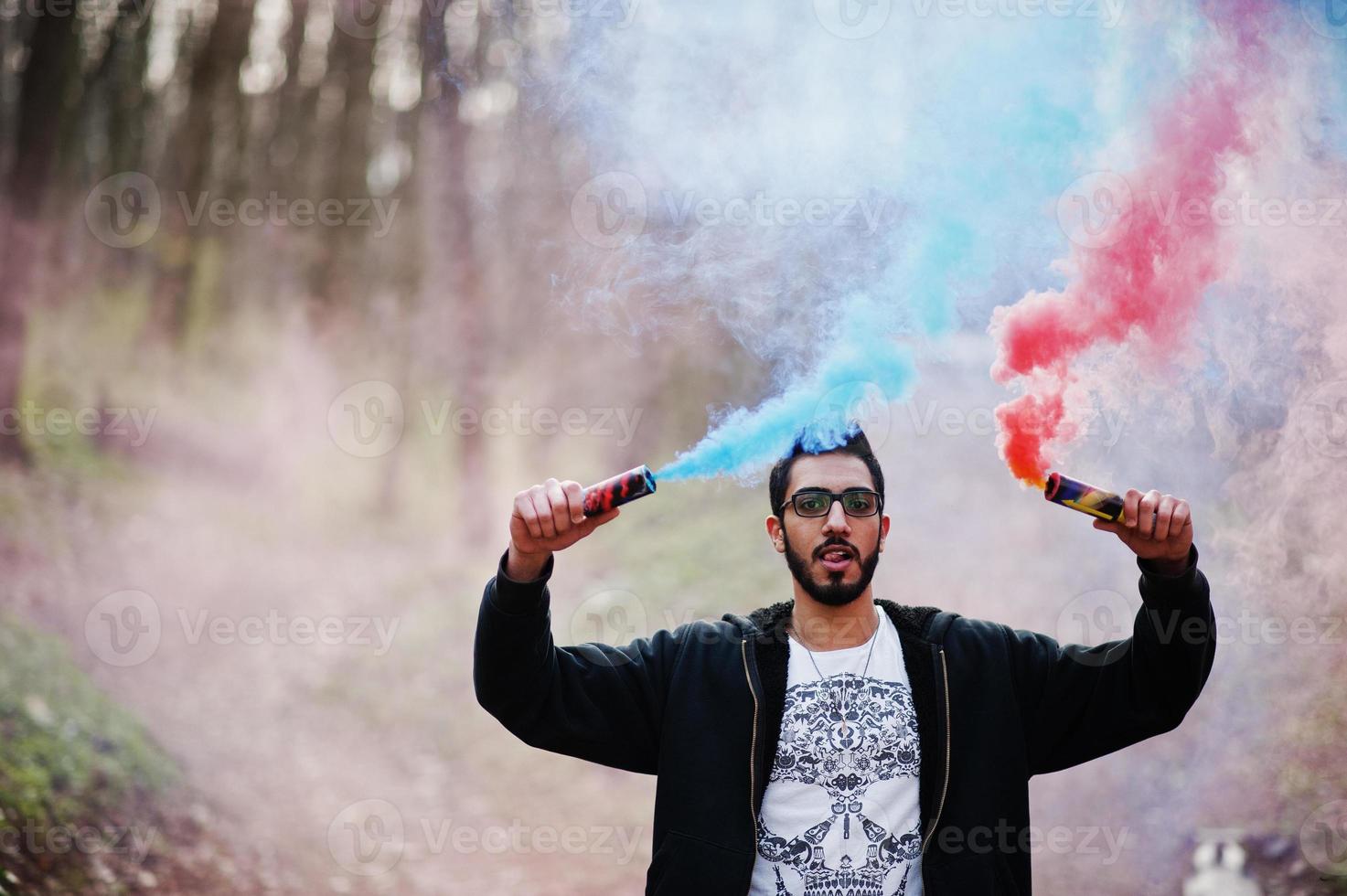 Street style arab man in eyeglasses hold hand flare with red and blue smoke grenade bomb. photo