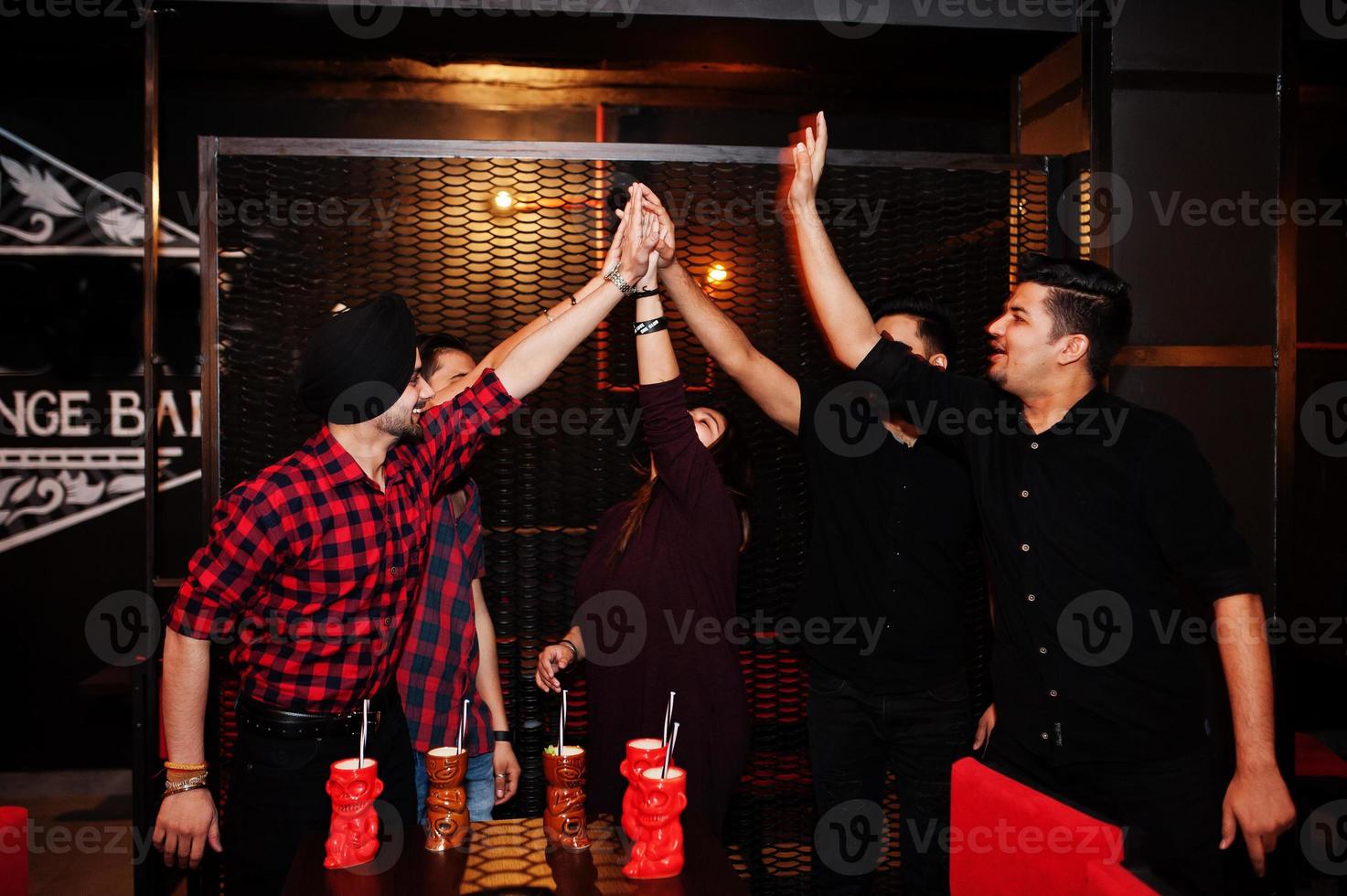 Group of indian friends having fun and rest at night club, drinking cocktails and giving high five together. photo