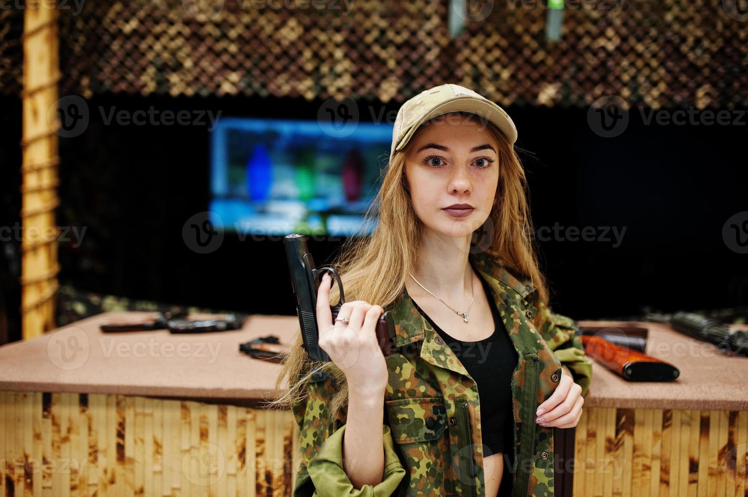 Military girl in camouflage uniform with gun at hand against army background on shooting range. photo