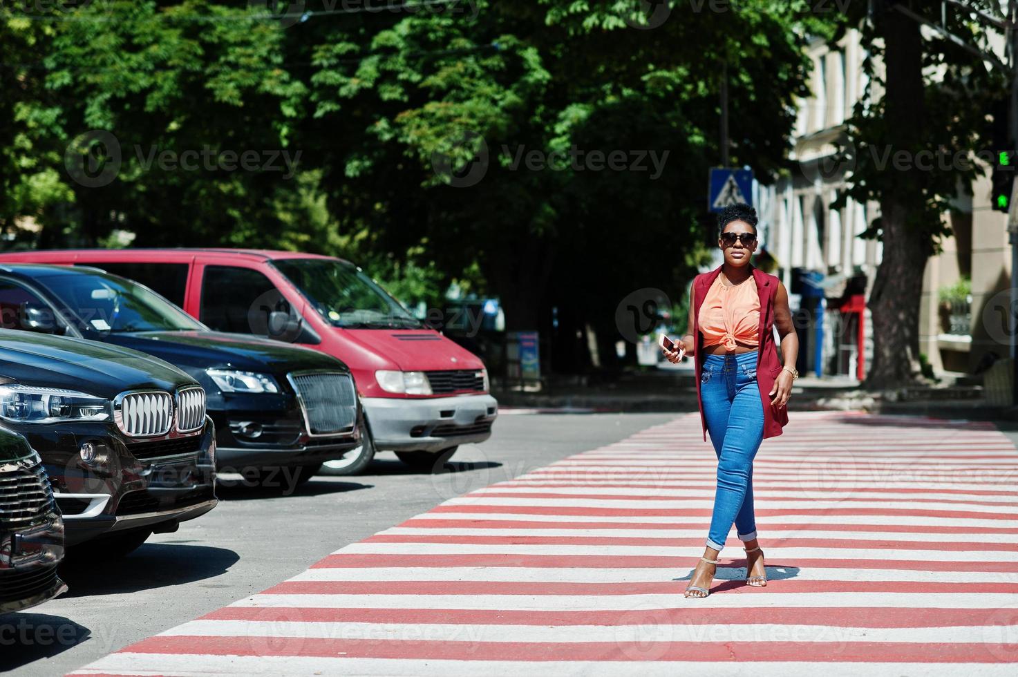 elegante mujer afroamericana caminando en el paso de peatones o en el paso de peatones con el teléfono móvil a mano. foto