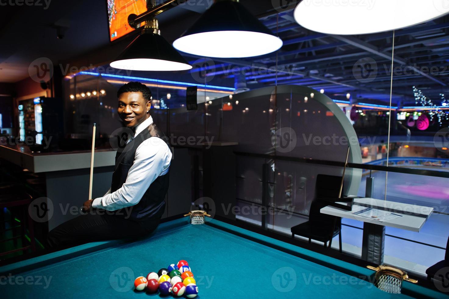 Young handsome african man wearing white shirt, black vest and bow tie play pool billiard. photo