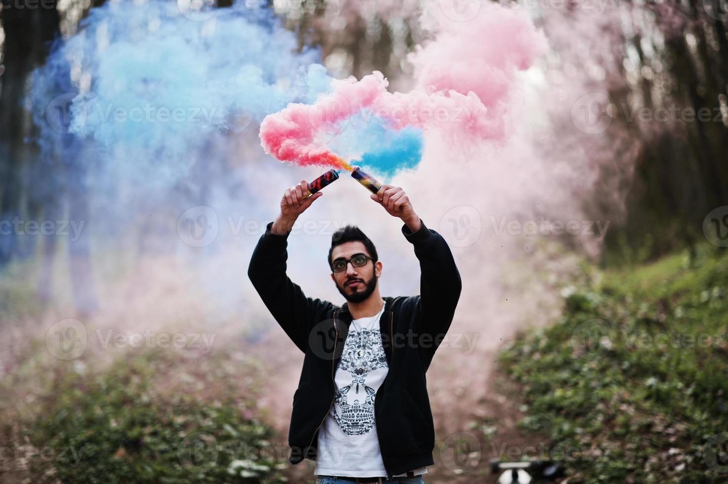 Street style arab man in eyeglasses hold hand flare with red and blue smoke grenade bomb. photo