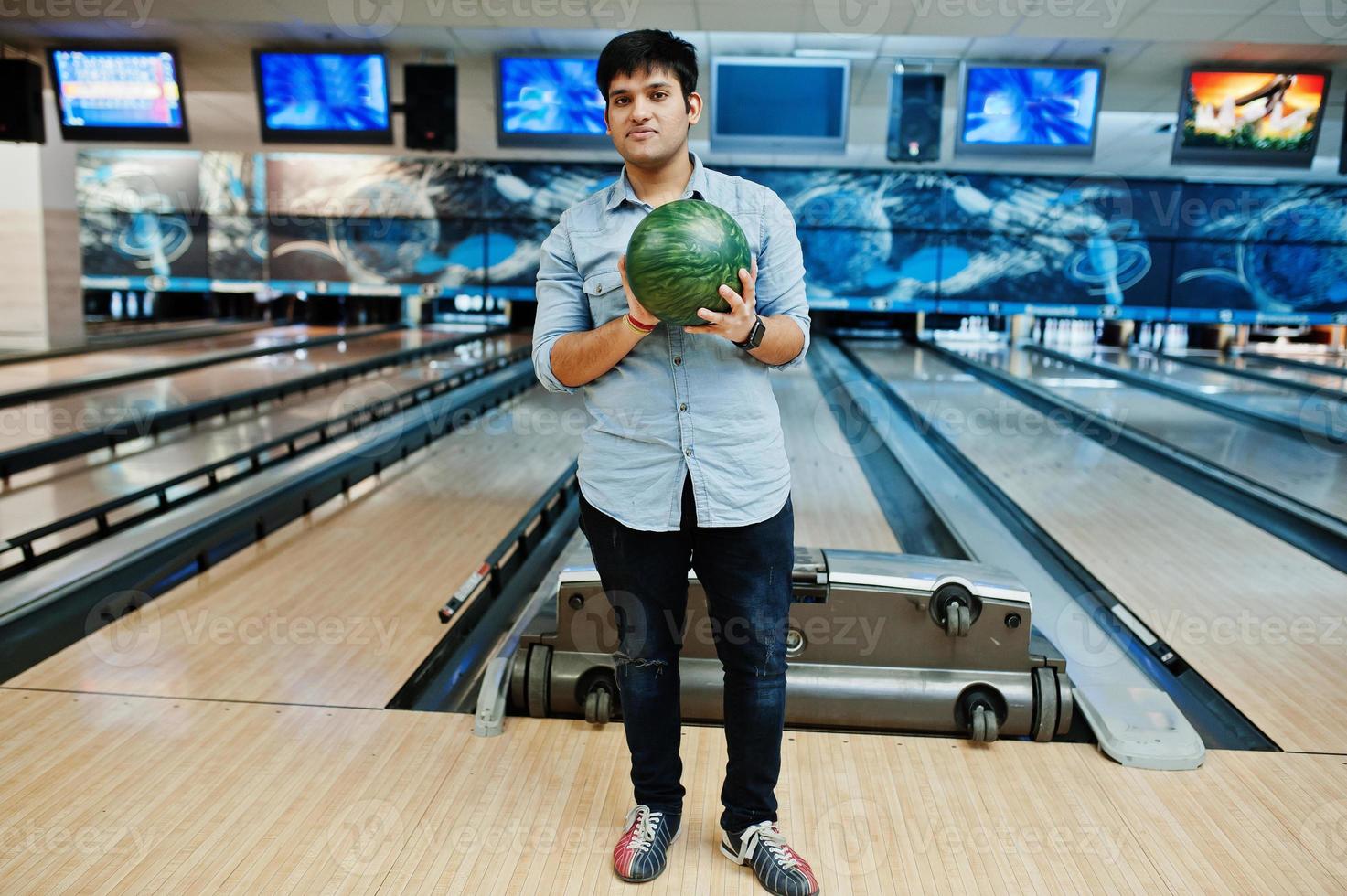 hombre asiático con estilo en camisa de jeans de pie en la bolera con la pelota en la mano. foto