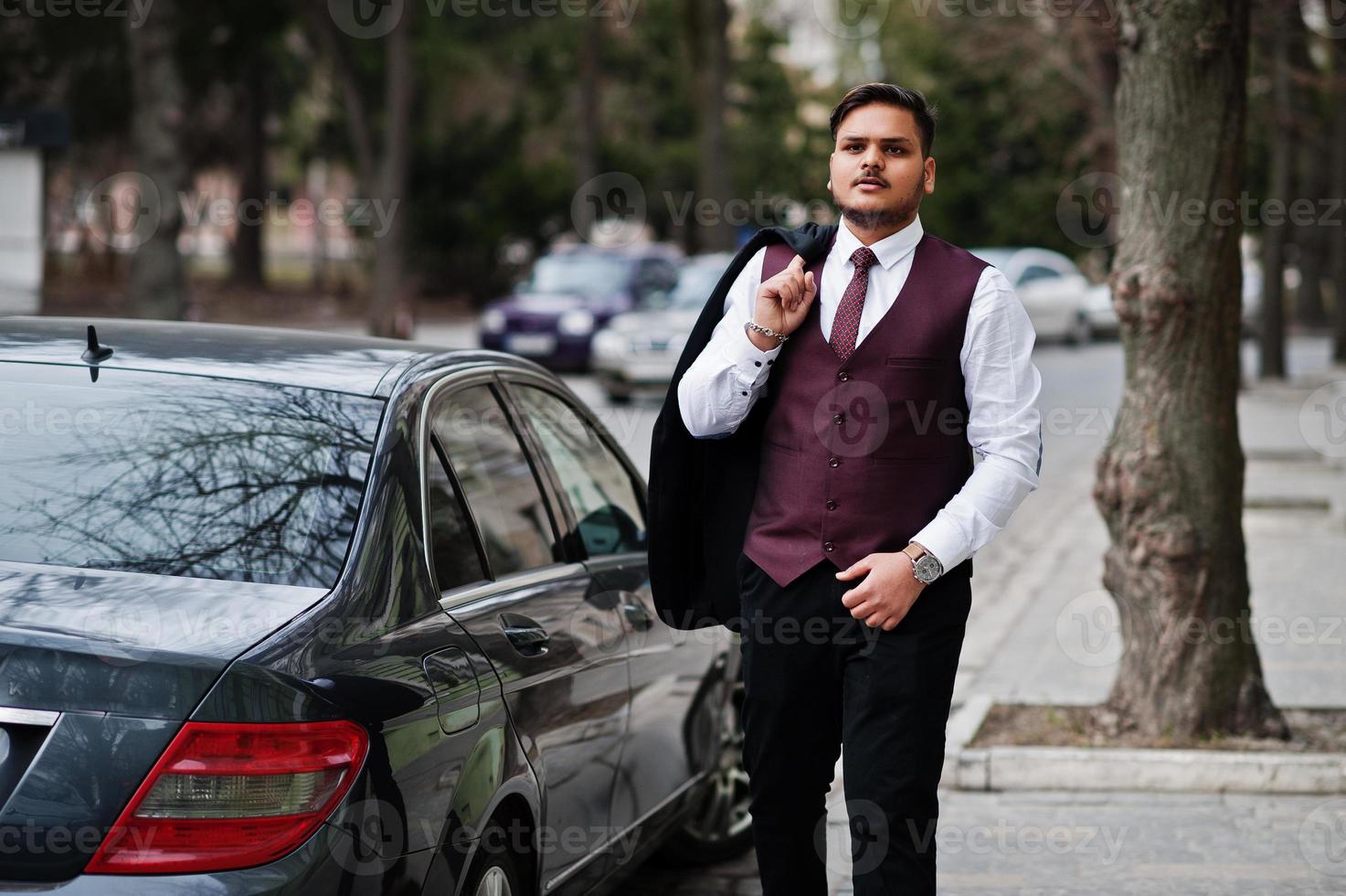 Stylish indian businessman in formal wear standing against black business car on street of city. photo