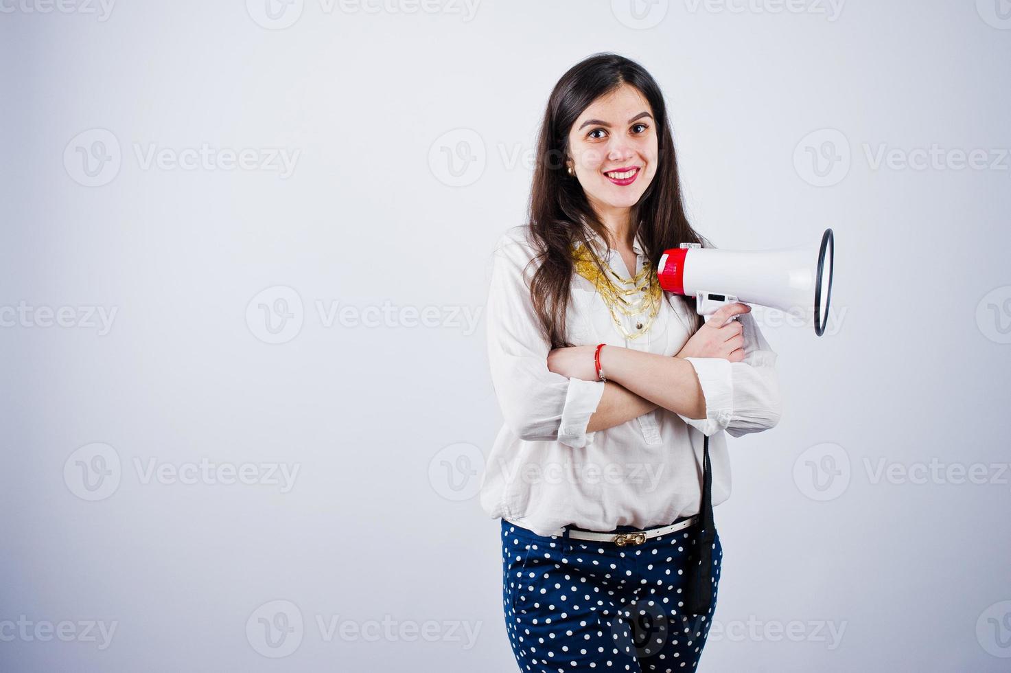 Portrait of a young woman in blue trousers and white blouse posing with megaphone in the studio. photo