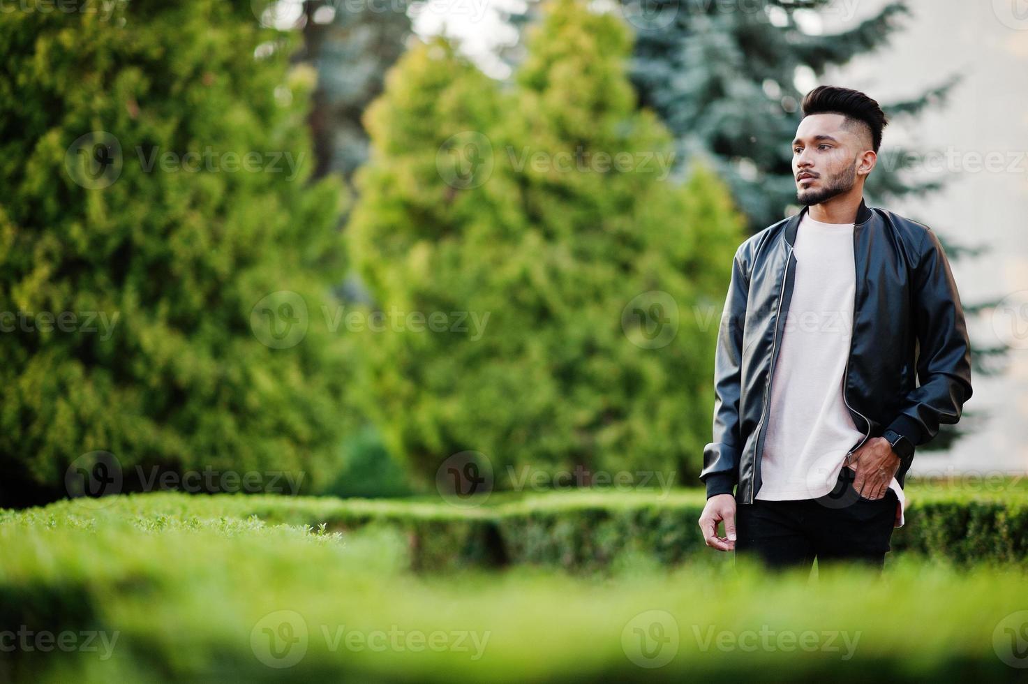 elegante hombre de barba india con chaqueta de cuero negro. modelo india posó en el jardín verde de la ciudad. foto